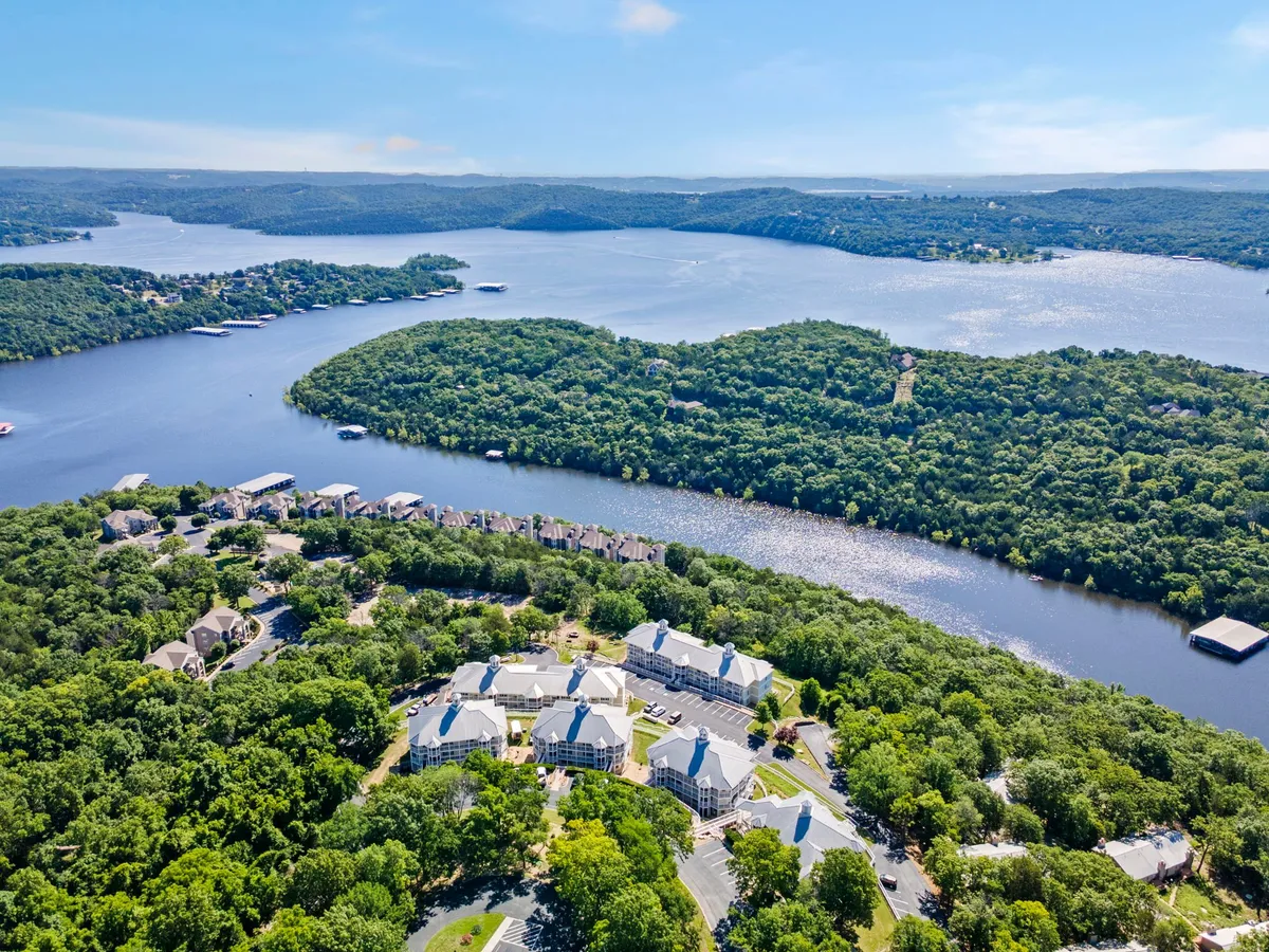 A wide, serene waterfront with green rolling hills and scattered residential buildings creates a peaceful lakeside scene. The area feels private and untouched, ideal for quiet moments and enjoying nature’s beauty together.
