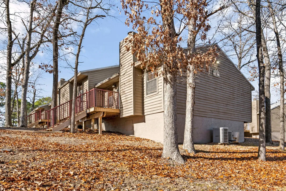 A peaceful wooden deck surrounded by tall trees and scattered fallen leaves. The scene invites moments of relaxation, with the natural beauty of the woodland providing a tranquil backdrop. Outdoor seating is visible, creating a welcoming spot for gatherings or quiet reflection.