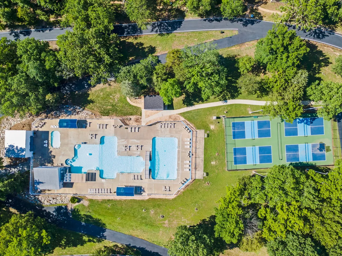 An inviting outdoor scene featuring a sparkling swimming pool surrounded by lounge chairs, with tennis courts and lush greenery in the background. The space is designed for both relaxation and play, offering opportunities for swimming, sunbathing, and tennis in a vibrant, family-friendly environment.