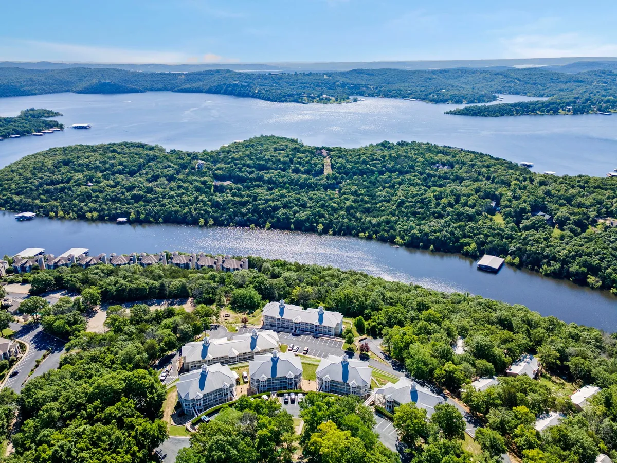 A panoramic view of Table Rock Lake framed by forest, with residential buildings and a visible river. The setting is peaceful yet brimming with potential for hiking, boating, and exploring the outdoors.