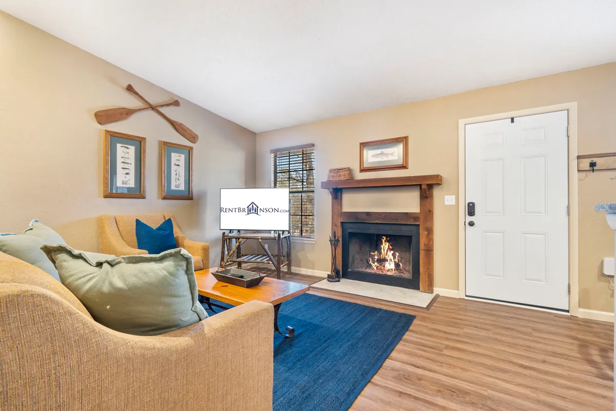 A welcoming living area featuring a cozy fireplace, plush sofa, a coffee table, and decorative paddles on the wall. The space glows with soft, warm lighting, inviting guests to relax, socialize, or curl up with a book.
