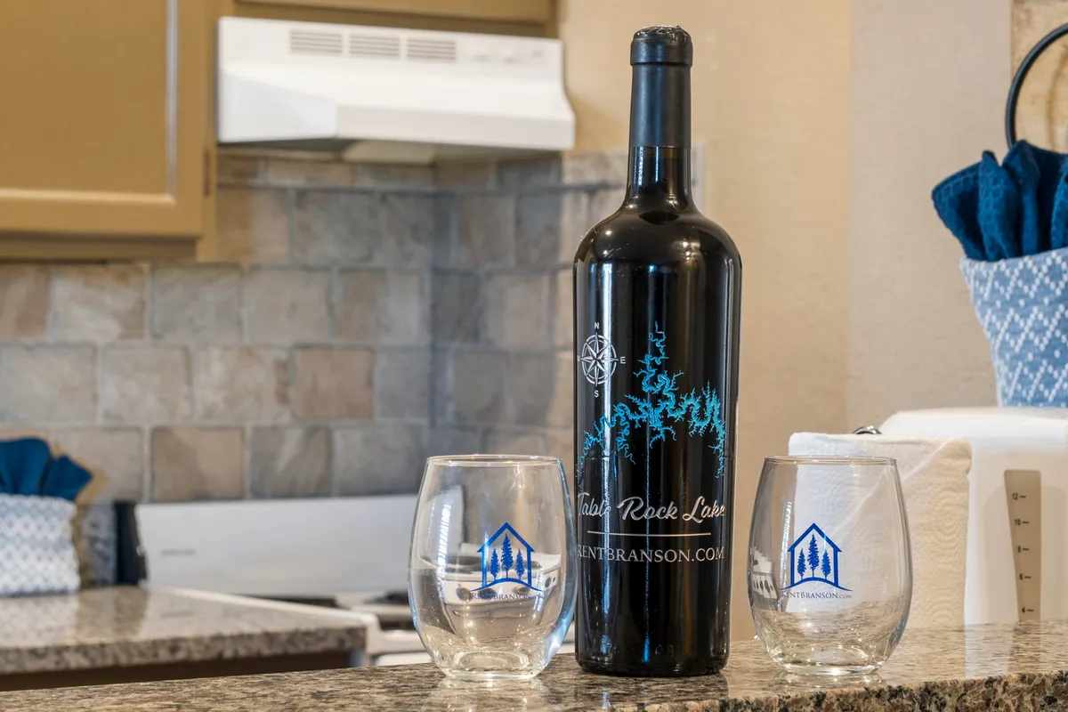 A bottle of wine and two glasses are set on a kitchen counter, with a relaxed, softly lit atmosphere in the background. The scene is intimate, suggesting a cozy evening in for two.
