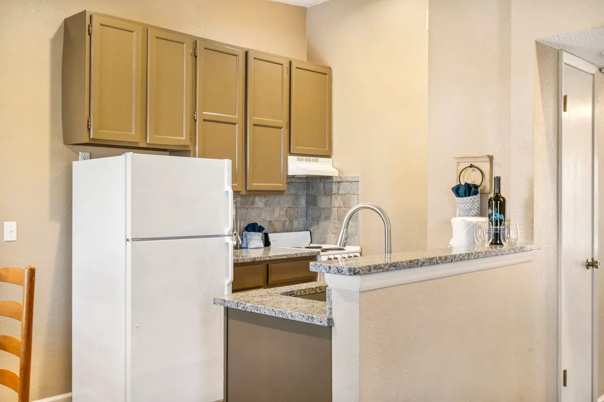 A close-up of the kitchen area featuring granite countertops, a white refrigerator, and classic kitchen cabinets. The scene is set for culinary creativity and family-style entertaining, with everything needed for memorable meals.