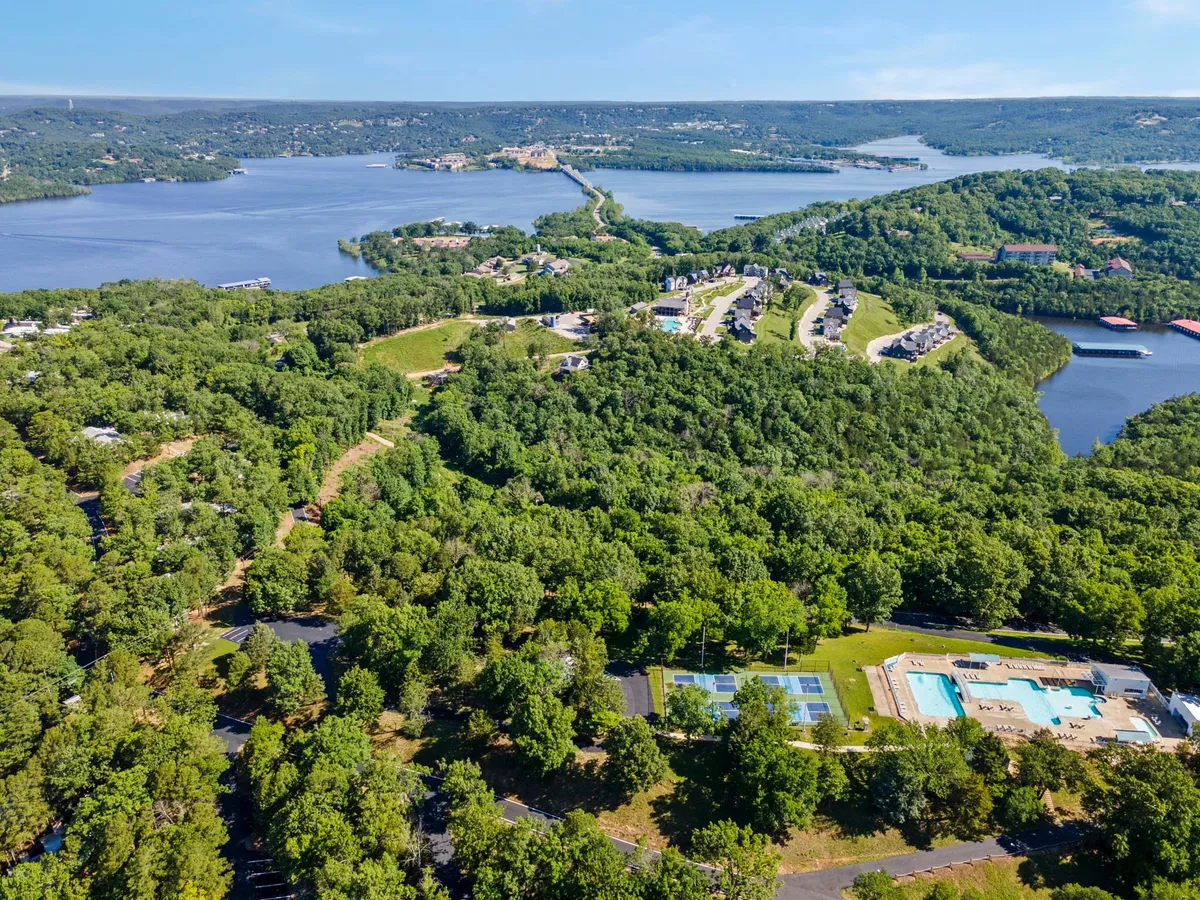 A sweeping view of Pine Ridge resort’s outdoor amenities, featuring sparkling lake waters, lush trees, a swimming pool area, tennis courts, and scenic homes on the hillsides. The landscape suggests ample space for outdoor activities, relaxation, and family fun.