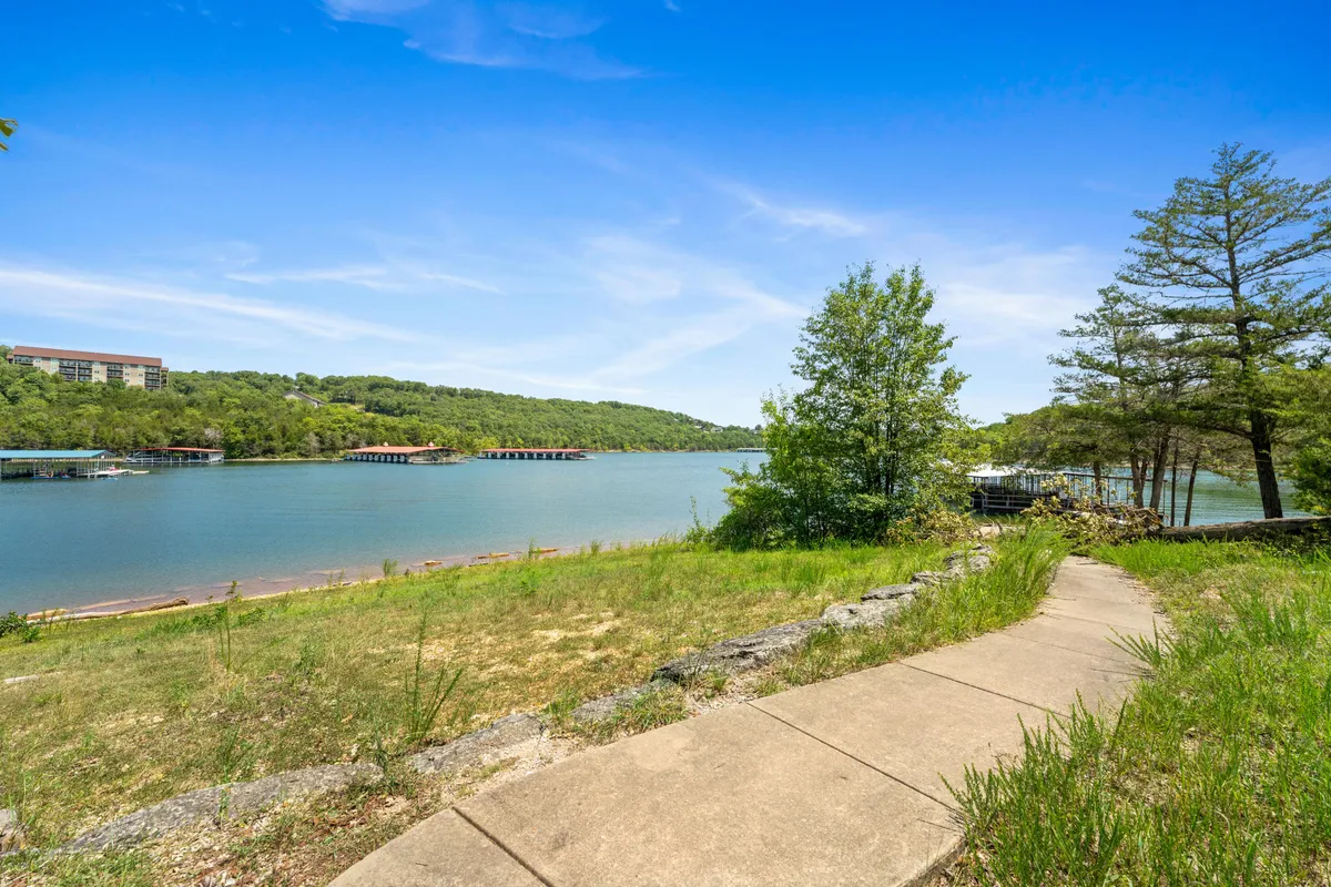 A tranquil lakeside scene with a wide pathway meandering beside a calm lake, surrounded by lush greenery and distant hills. The gently curving trail is perfect for walking with a pet, and the open space invites outdoor exploration and relaxation.